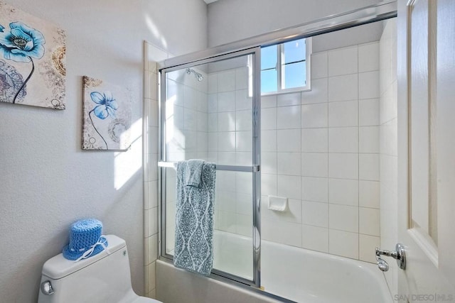 bathroom featuring toilet and bath / shower combo with glass door