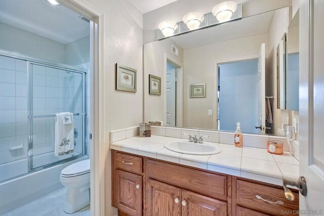 full bathroom featuring bath / shower combo with glass door, vanity, and toilet