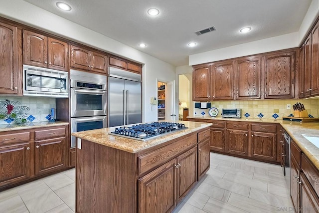 kitchen featuring tasteful backsplash, built in appliances, light stone countertops, and a kitchen island