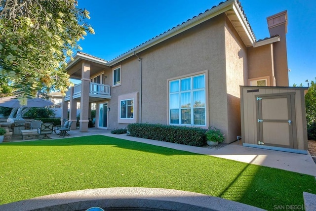 rear view of house featuring a balcony, a lawn, a patio area, and a shed