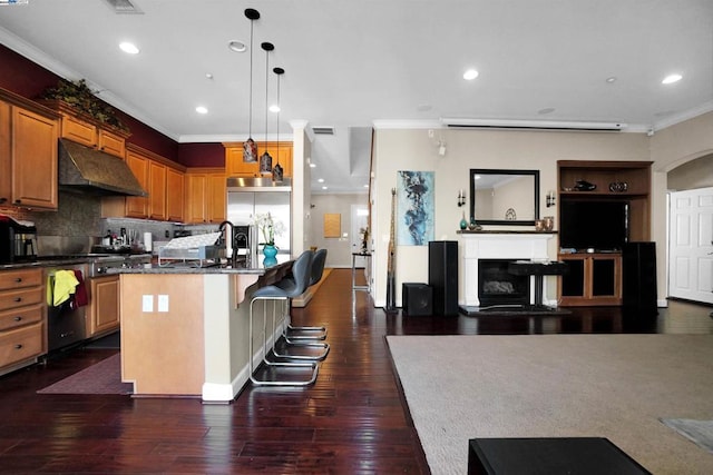 kitchen with an island with sink, hanging light fixtures, dark hardwood / wood-style floors, and ornamental molding