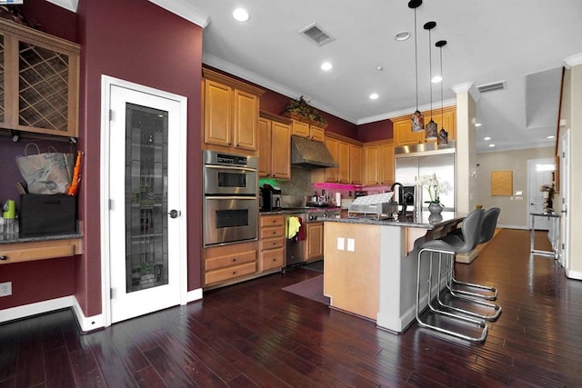 kitchen featuring dark hardwood / wood-style floors, double oven, an island with sink, pendant lighting, and a kitchen bar