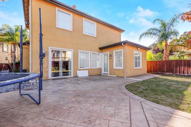 back of house with a patio, a trampoline, and a lawn