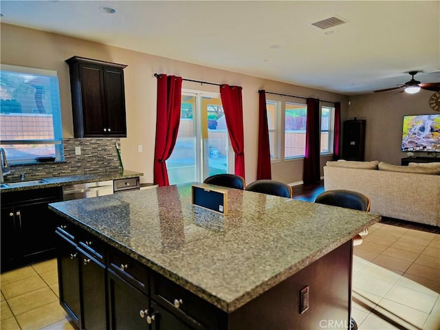 kitchen featuring stone counters, sink, ceiling fan, light tile patterned flooring, and a kitchen island