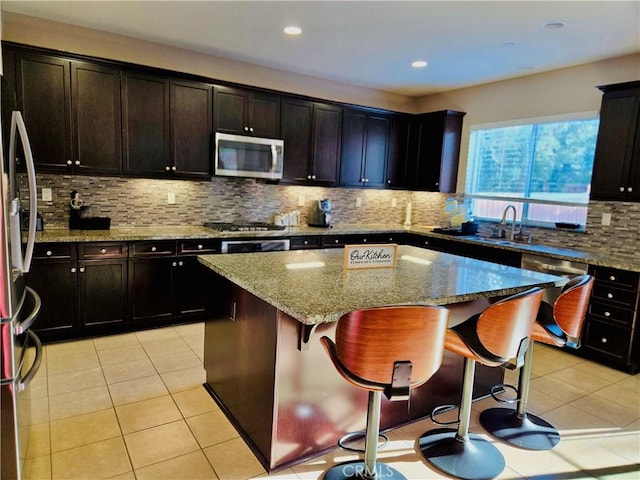 kitchen featuring appliances with stainless steel finishes, backsplash, light stone counters, a center island, and a breakfast bar area