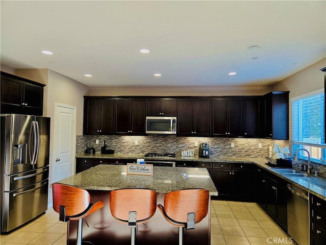 kitchen with appliances with stainless steel finishes, light stone counters, sink, a center island, and a breakfast bar area