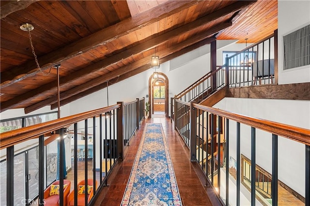 corridor with lofted ceiling with beams, a healthy amount of sunlight, dark hardwood / wood-style flooring, and wooden ceiling