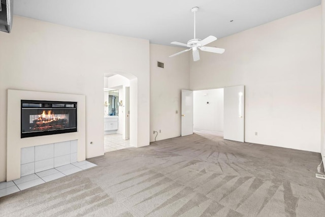 unfurnished living room featuring ceiling fan, a towering ceiling, and light carpet