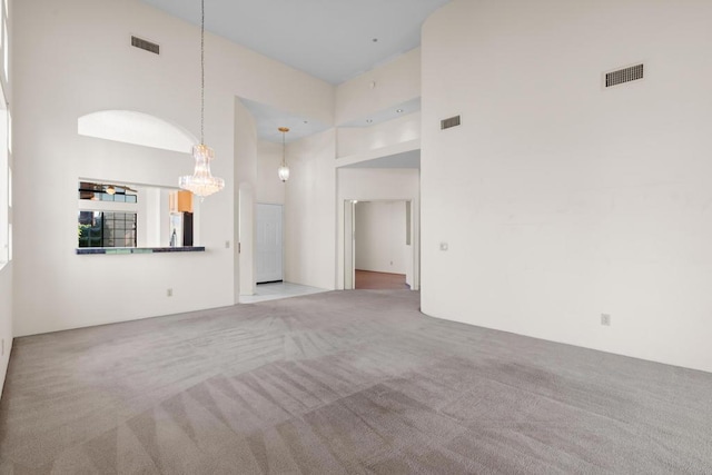 unfurnished living room featuring a notable chandelier, light carpet, and a high ceiling