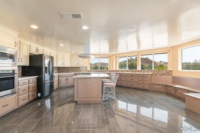 kitchen with decorative backsplash, appliances with stainless steel finishes, island exhaust hood, a breakfast bar, and a center island