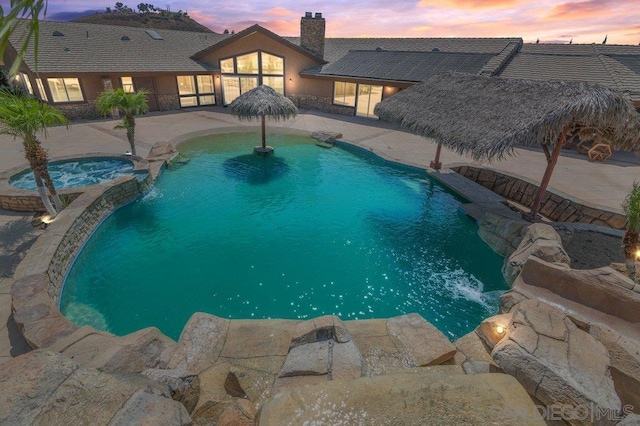 pool at dusk featuring an in ground hot tub and a patio