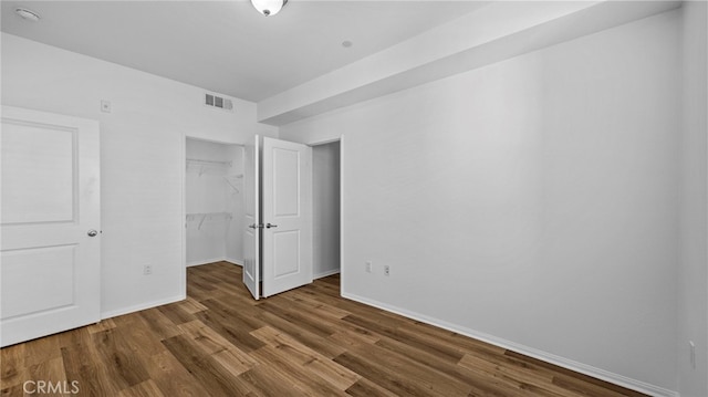 unfurnished bedroom with dark hardwood / wood-style flooring, a walk in closet, and a closet