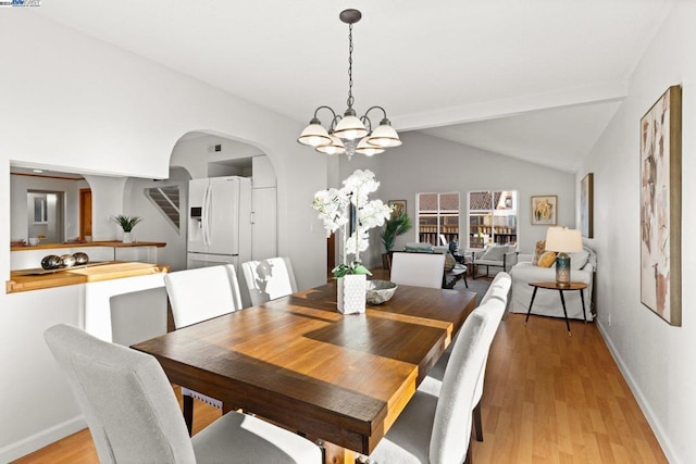 dining area featuring vaulted ceiling with beams, light hardwood / wood-style flooring, and an inviting chandelier