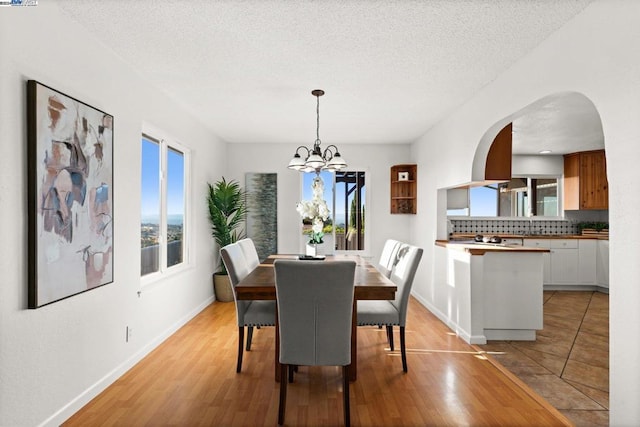 dining room featuring a notable chandelier, light hardwood / wood-style floors, a healthy amount of sunlight, and a textured ceiling