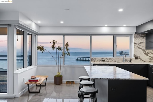 kitchen with a water view, sink, light stone countertops, tasteful backsplash, and a kitchen island