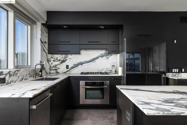 kitchen featuring backsplash, sink, light stone countertops, range hood, and stainless steel appliances