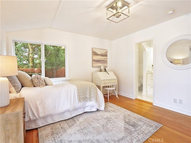 bedroom featuring hardwood / wood-style flooring, an inviting chandelier, lofted ceiling, and ensuite bath