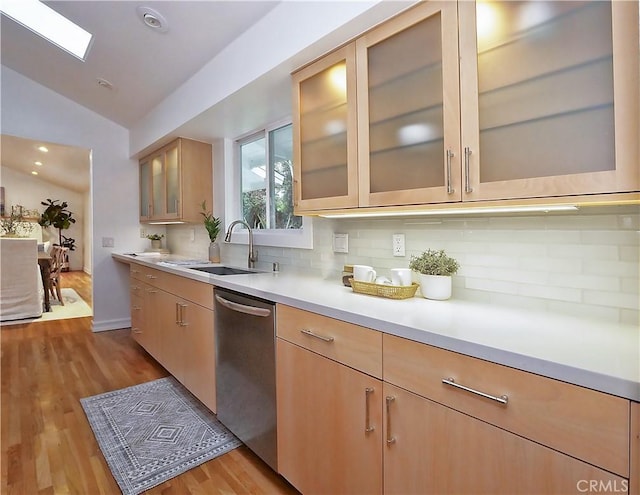 kitchen with dishwasher, lofted ceiling with skylight, sink, light brown cabinetry, and light hardwood / wood-style floors