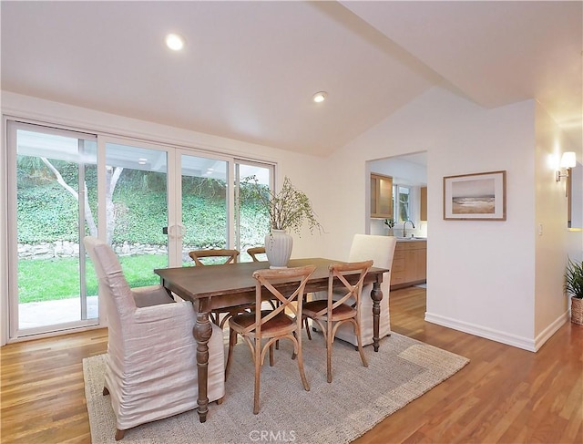 dining room featuring light wood-type flooring, sink, and vaulted ceiling