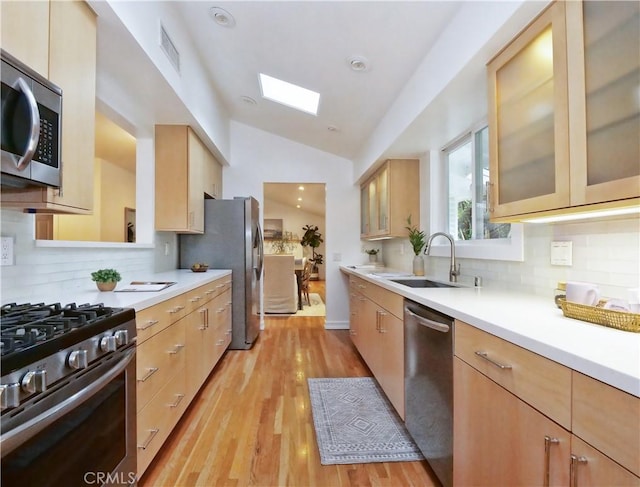 kitchen featuring lofted ceiling with skylight, sink, decorative backsplash, light hardwood / wood-style floors, and stainless steel appliances