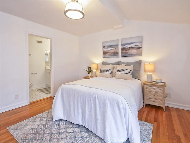 bedroom with wood-type flooring, connected bathroom, and vaulted ceiling