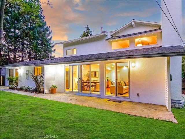 back house at dusk featuring a yard and a patio