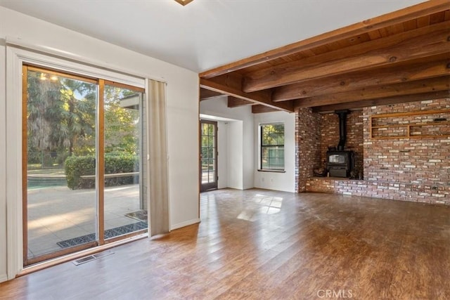 unfurnished living room featuring beam ceiling, a wood stove, a wealth of natural light, and hardwood / wood-style floors