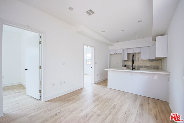 kitchen featuring kitchen peninsula, refrigerator, backsplash, light hardwood / wood-style flooring, and white cabinetry