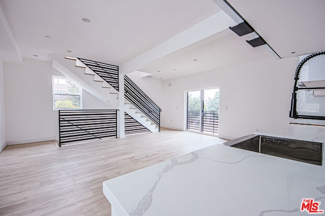 interior space featuring light stone countertops, beam ceiling, light wood-type flooring, and a healthy amount of sunlight