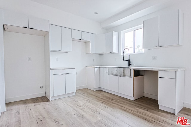 kitchen with light hardwood / wood-style floors, white cabinetry, and sink