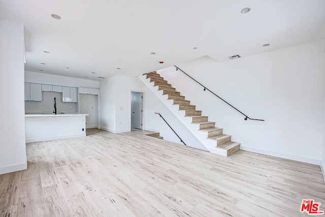 unfurnished living room with sink and light hardwood / wood-style floors