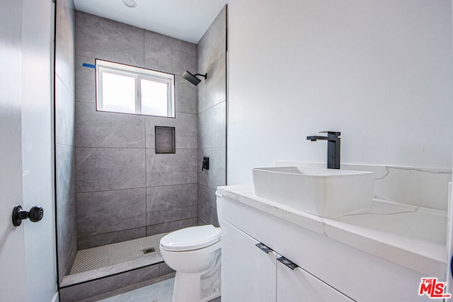 bathroom featuring a tile shower, vanity, and toilet