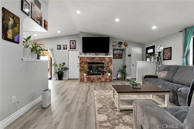 living room featuring a healthy amount of sunlight, light wood-type flooring, a fireplace, and vaulted ceiling