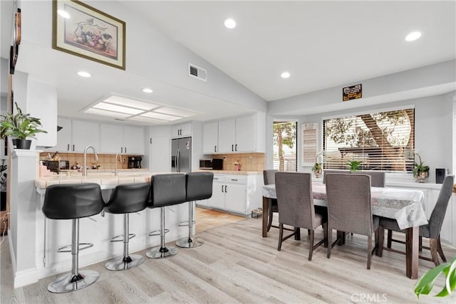 kitchen featuring stainless steel appliances, light hardwood / wood-style flooring, kitchen peninsula, vaulted ceiling, and white cabinets