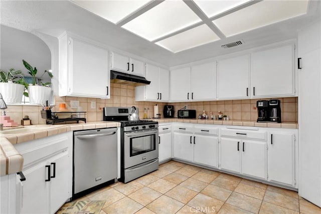 kitchen featuring stainless steel appliances, white cabinets, backsplash, tile countertops, and light tile patterned flooring