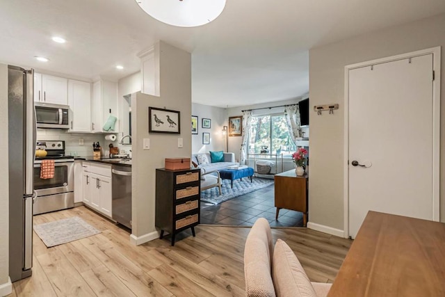 kitchen with white cabinets, appliances with stainless steel finishes, sink, backsplash, and light hardwood / wood-style flooring