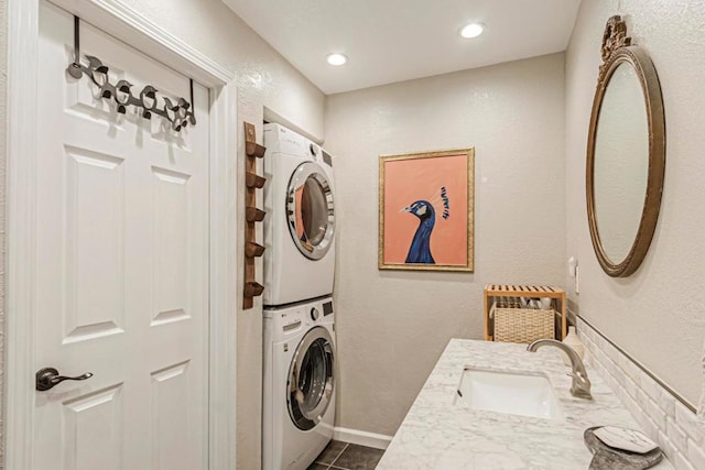 washroom with sink, dark tile patterned flooring, and stacked washer and clothes dryer