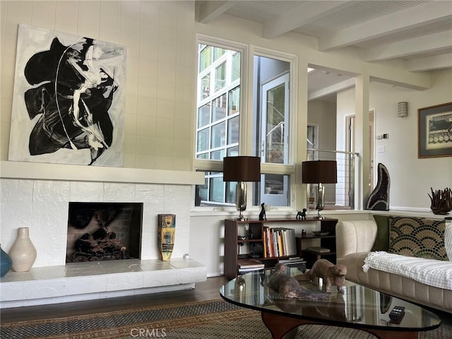 living room with beamed ceiling, wood-type flooring, and a tiled fireplace