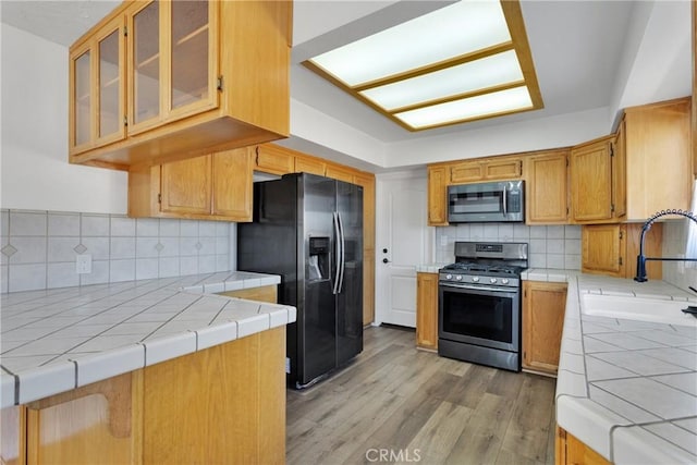 kitchen featuring backsplash, stainless steel appliances, sink, light hardwood / wood-style floors, and tile counters