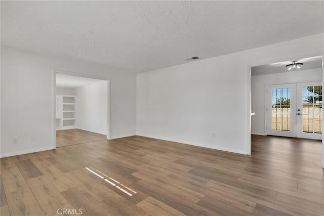 empty room featuring built in features, wood-type flooring, a textured ceiling, and french doors