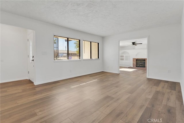 unfurnished living room featuring a fireplace, a textured ceiling, light wood-type flooring, and ceiling fan