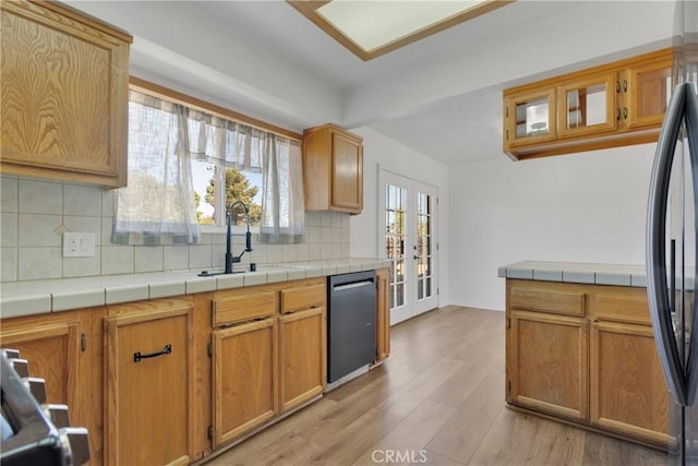 kitchen with decorative backsplash, appliances with stainless steel finishes, light hardwood / wood-style floors, and tile counters