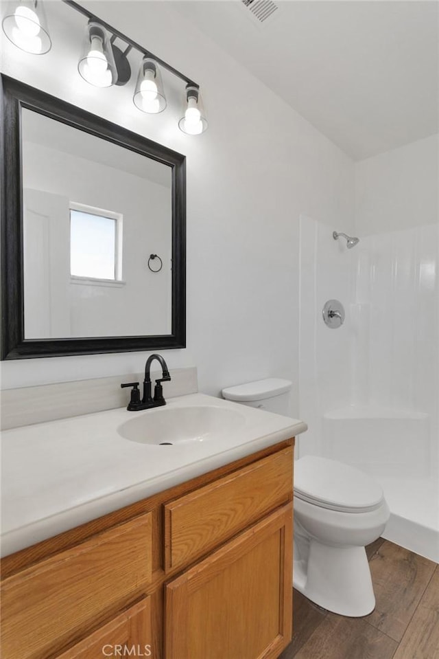 bathroom with a tile shower, toilet, vanity, and hardwood / wood-style flooring