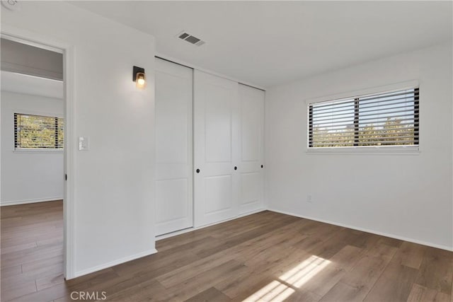 unfurnished bedroom with hardwood / wood-style floors, a closet, and multiple windows