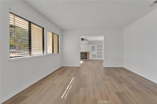 unfurnished living room featuring built in features, light hardwood / wood-style floors, a brick fireplace, and ceiling fan