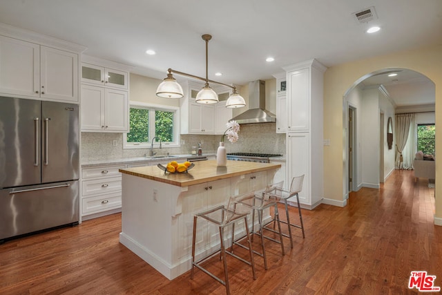 kitchen with high quality fridge, white cabinetry, a center island, and wall chimney range hood