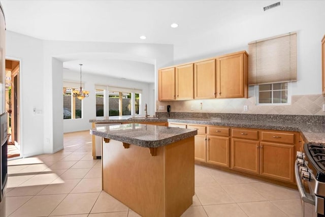 kitchen featuring a kitchen breakfast bar, backsplash, high end stove, a notable chandelier, and hanging light fixtures