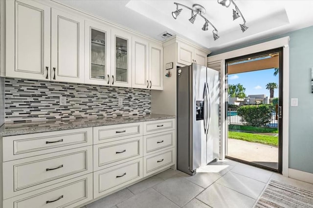 kitchen with stainless steel refrigerator with ice dispenser, light tile patterned floors, tasteful backsplash, and light stone counters