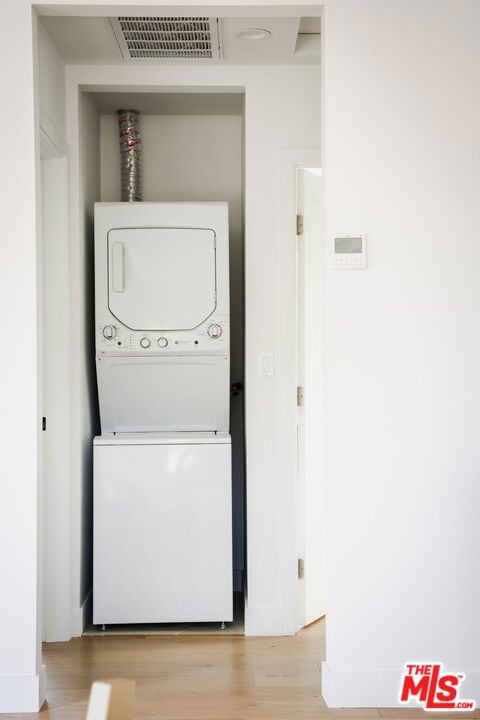 clothes washing area with light hardwood / wood-style floors and stacked washer and clothes dryer