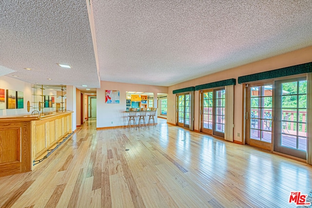 unfurnished living room with sink, light wood-type flooring, and a textured ceiling